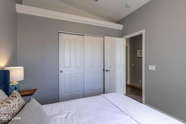 bedroom with vaulted ceiling, a closet, wood finished floors, and baseboards