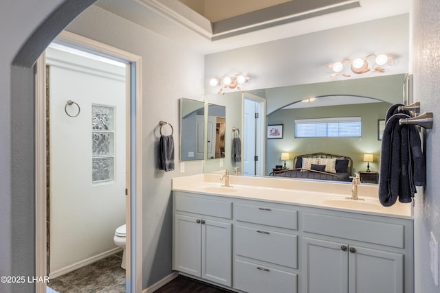 ensuite bathroom with double vanity, a sink, toilet, and connected bathroom