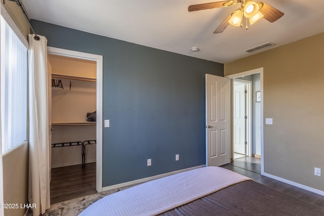 bedroom with baseboards, dark wood finished floors, visible vents, a walk in closet, and a closet