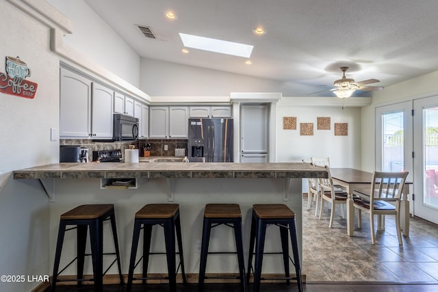 kitchen featuring a breakfast bar, dark countertops, a peninsula, and stainless steel refrigerator with ice dispenser