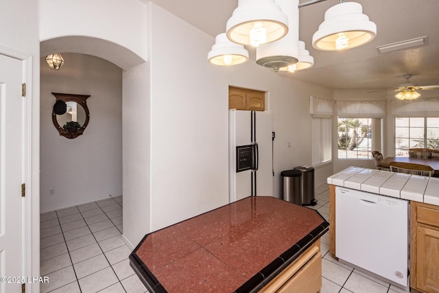 kitchen with white appliances, light tile patterned floors, visible vents, tile counters, and arched walkways