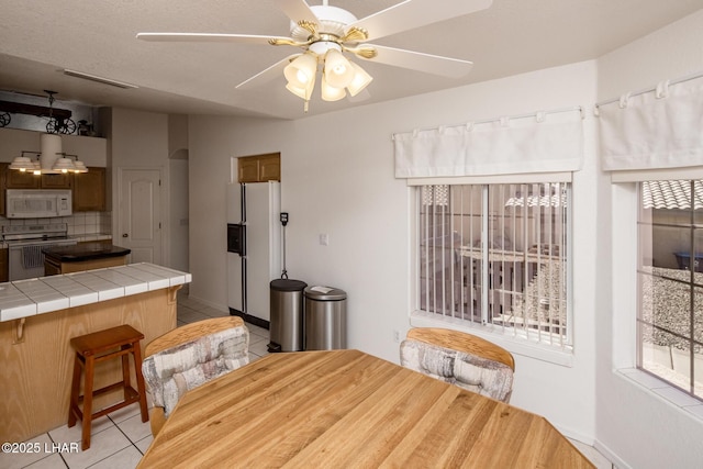 dining room featuring a ceiling fan, a wealth of natural light, visible vents, and light tile patterned floors