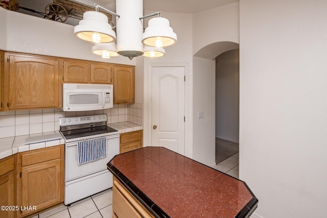 kitchen with white appliances, light tile patterned floors, tile counters, arched walkways, and backsplash