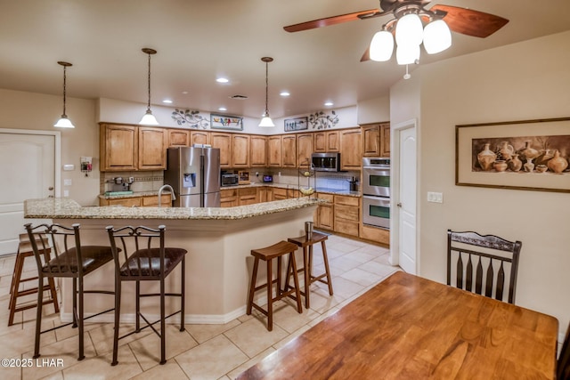 kitchen featuring tasteful backsplash, a breakfast bar, brown cabinetry, stainless steel appliances, and a ceiling fan