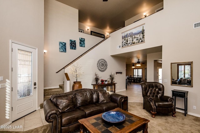 living room featuring light carpet, a towering ceiling, stairway, light tile patterned flooring, and ceiling fan