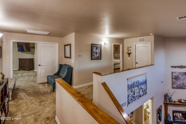 hallway with an upstairs landing, visible vents, light colored carpet, and baseboards