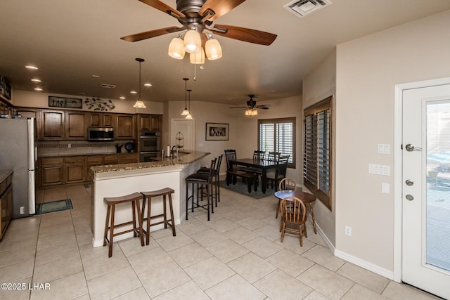 kitchen with visible vents, a center island with sink, appliances with stainless steel finishes, a kitchen breakfast bar, and a ceiling fan