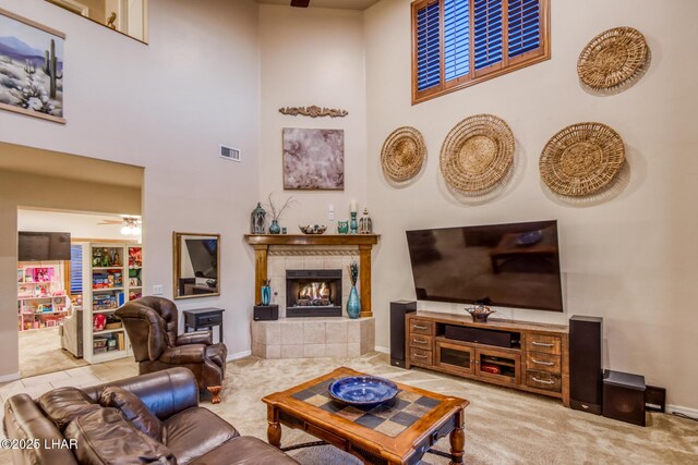 living area with visible vents, carpet floors, a fireplace, ceiling fan, and a towering ceiling