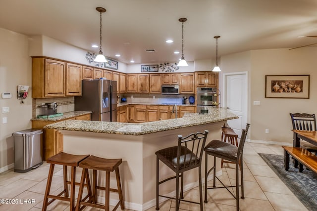 kitchen with light tile patterned floors, backsplash, appliances with stainless steel finishes, and a breakfast bar area