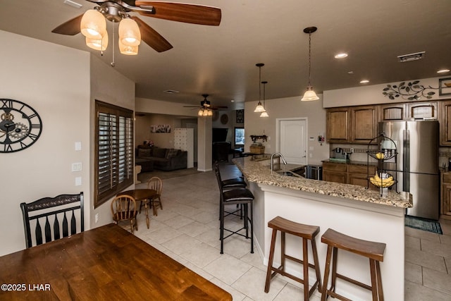 kitchen with visible vents, a breakfast bar, freestanding refrigerator, light tile patterned flooring, and a ceiling fan