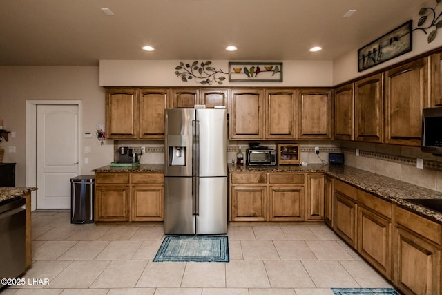 kitchen featuring brown cabinetry, backsplash, appliances with stainless steel finishes, and dark stone counters