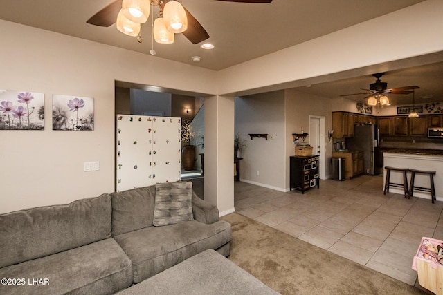 living area featuring light colored carpet, light tile patterned floors, a ceiling fan, and baseboards