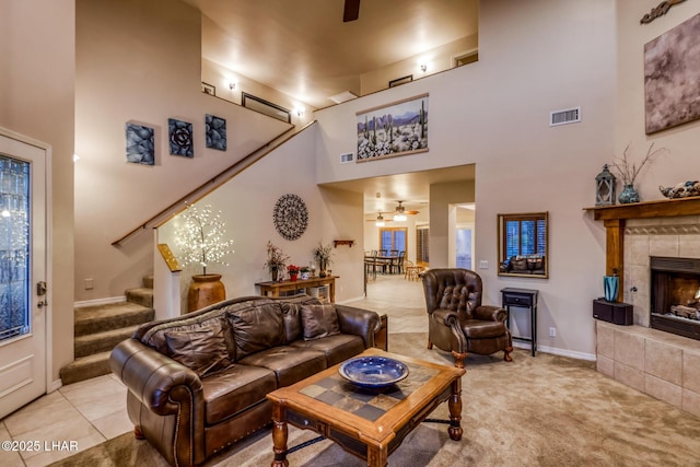 living area with stairway, a ceiling fan, visible vents, a towering ceiling, and light carpet