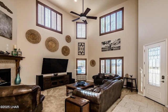 living area with baseboards, a tile fireplace, a towering ceiling, light tile patterned flooring, and a ceiling fan