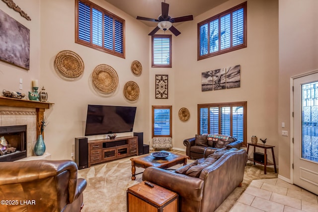 tiled living area featuring a tiled fireplace, baseboards, ceiling fan, and a towering ceiling