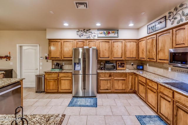 kitchen featuring light stone counters, visible vents, appliances with stainless steel finishes, brown cabinets, and backsplash