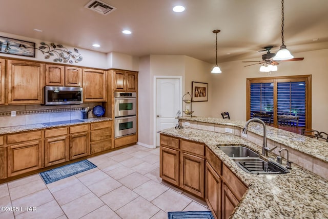 kitchen with visible vents, ceiling fan, appliances with stainless steel finishes, brown cabinetry, and a sink