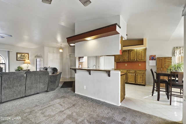 kitchen with a breakfast bar area, white refrigerator, tasteful backsplash, light carpet, and kitchen peninsula