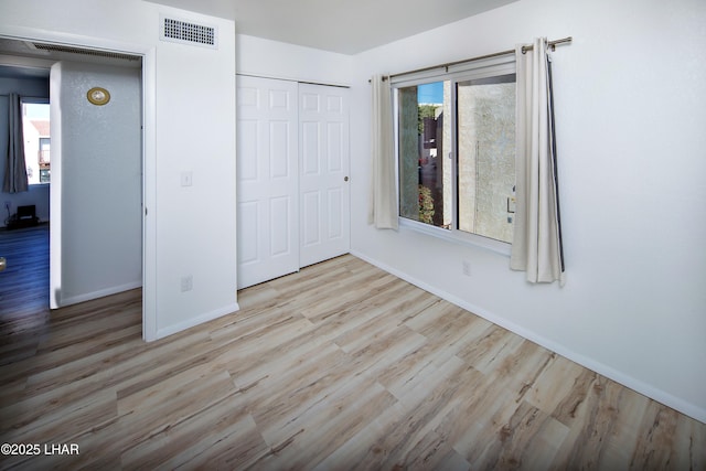 unfurnished bedroom with visible vents, baseboards, a closet, and wood finished floors