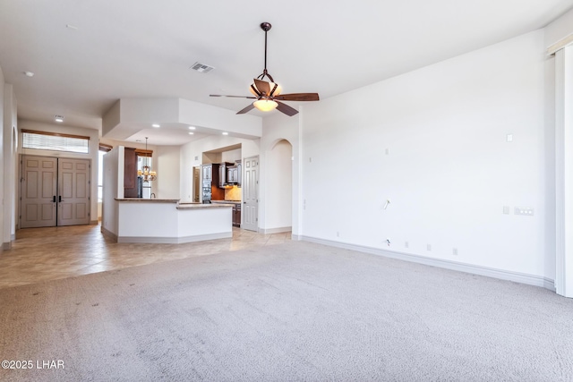 unfurnished living room with arched walkways, baseboards, visible vents, light colored carpet, and ceiling fan