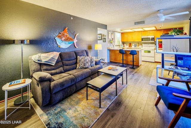 living room featuring ceiling fan, light hardwood / wood-style flooring, and a textured ceiling