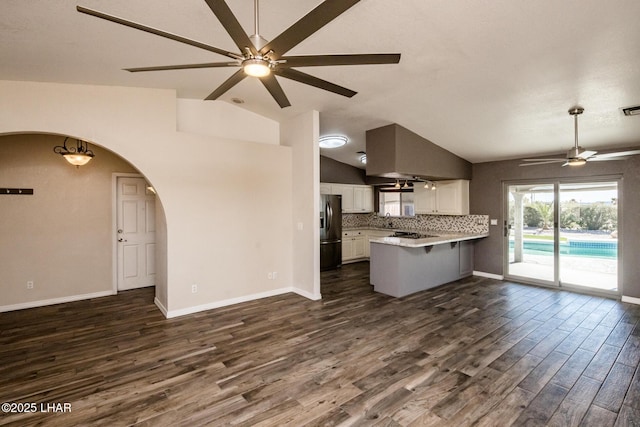 kitchen featuring dark wood-type flooring, stainless steel refrigerator, white cabinets, vaulted ceiling, and kitchen peninsula