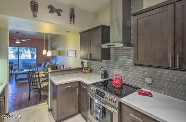 kitchen featuring wall chimney range hood, light countertops, a ceiling fan, stainless steel range with electric cooktop, and decorative backsplash