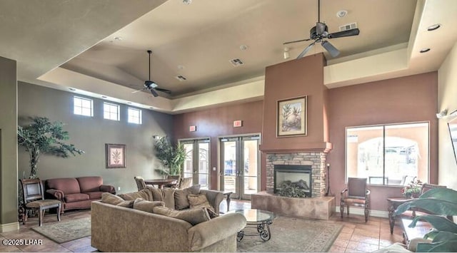 tiled living area with ceiling fan, a raised ceiling, a towering ceiling, and baseboards