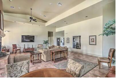 living room with high vaulted ceiling, visible vents, a stone fireplace, and a ceiling fan