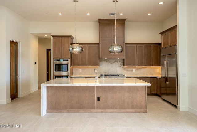 kitchen with pendant lighting, sink, backsplash, a kitchen island with sink, and stainless steel appliances