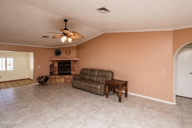 living room with vaulted ceiling, a textured ceiling, ornamental molding, ceiling fan, and a fireplace