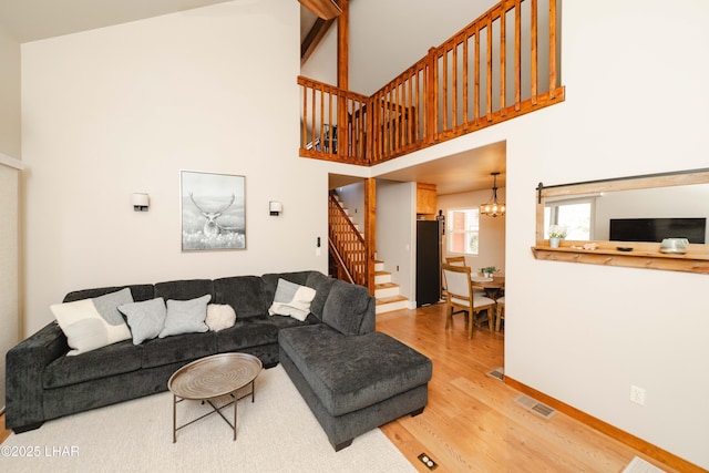 living room with visible vents, an inviting chandelier, wood finished floors, a high ceiling, and stairway