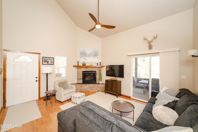 living area featuring light wood-style floors, a ceiling fan, a glass covered fireplace, and high vaulted ceiling