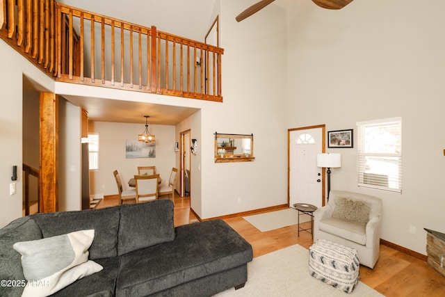 living area featuring baseboards, a high ceiling, wood finished floors, and ceiling fan with notable chandelier