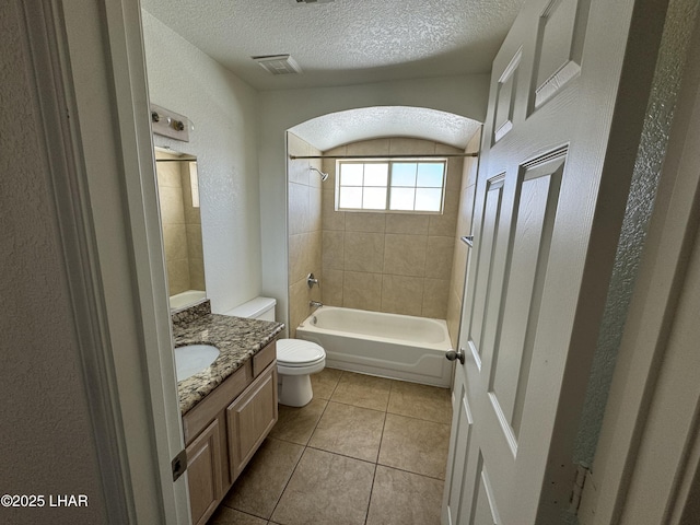 full bathroom featuring tiled shower / bath, vanity, toilet, tile patterned floors, and a textured ceiling