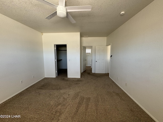 unfurnished bedroom featuring a spacious closet, ceiling fan, dark carpet, a textured ceiling, and a closet