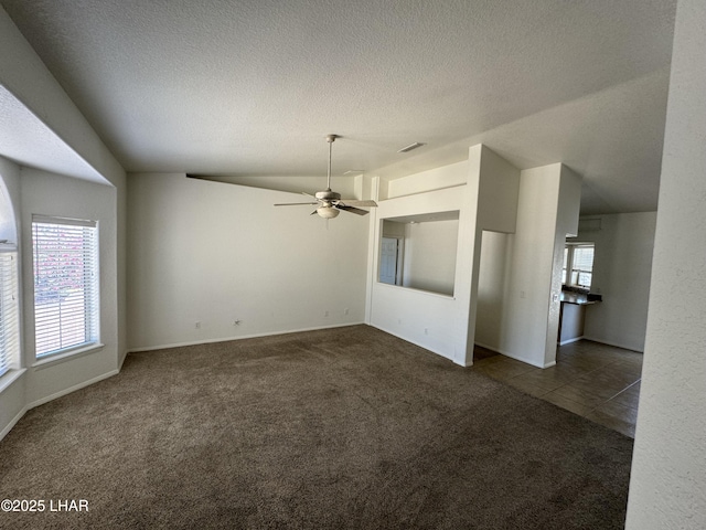 unfurnished living room featuring ceiling fan, dark carpet, vaulted ceiling, and a textured ceiling