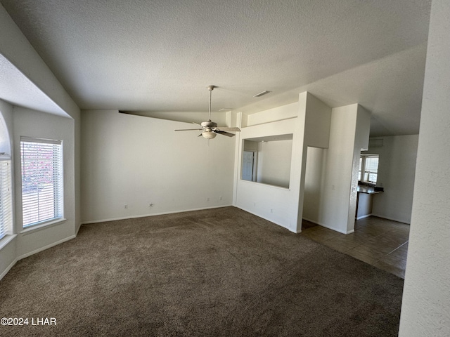 unfurnished living room with ceiling fan, vaulted ceiling, a textured ceiling, and dark colored carpet