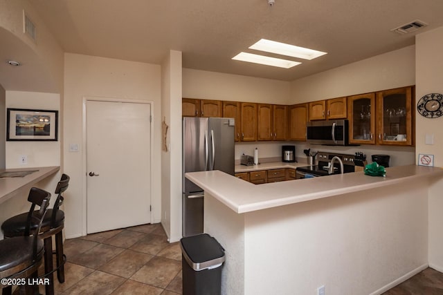 1650 S Smoketree Ave Unit 103, Lake Havasu City, AZ 86403 - kitchen with stainless steel appliances, brown cabinetry, glass insert cabinets, light countertops, and a peninsula