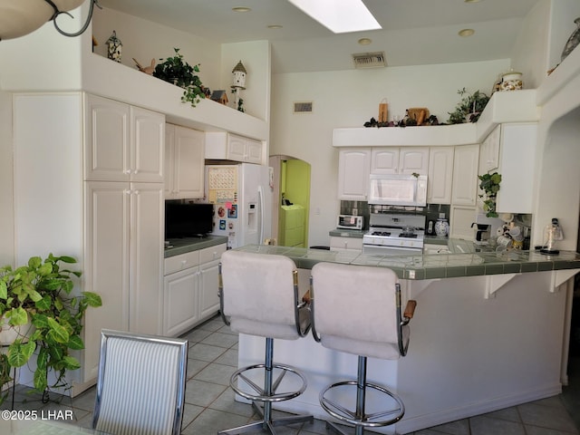 kitchen featuring a breakfast bar, washer and clothes dryer, white cabinetry, white appliances, and a peninsula