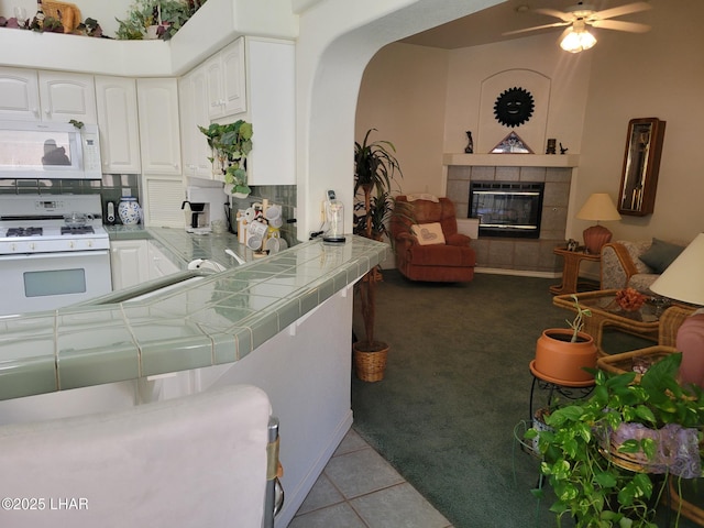 kitchen with light tile patterned flooring, white appliances, white cabinets, tile counters, and a tiled fireplace