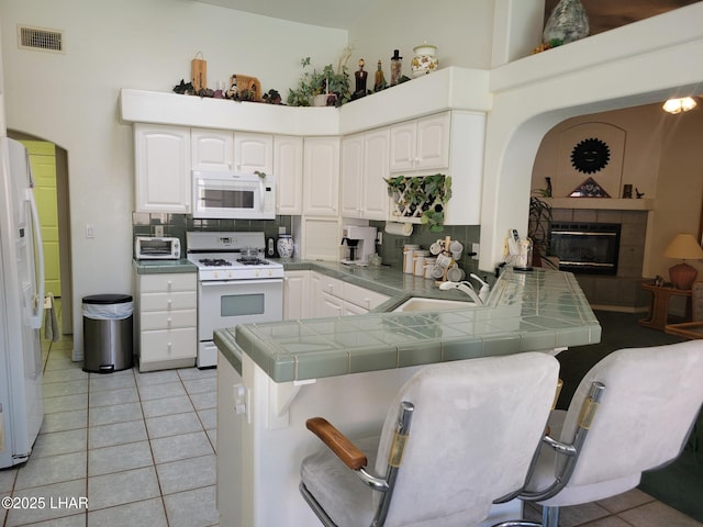 kitchen featuring tile countertops, white appliances, a peninsula, and white cabinets