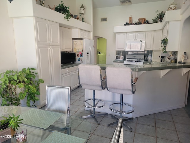 kitchen with white appliances, white cabinets, a peninsula, and a kitchen bar