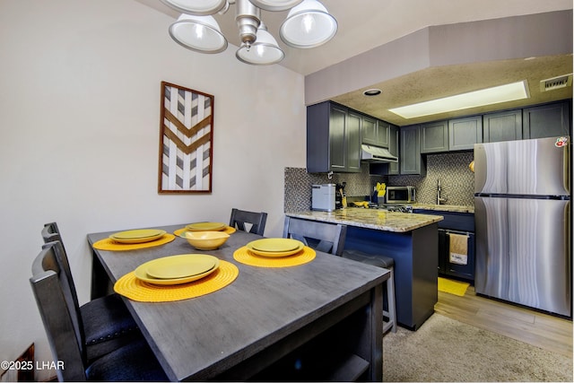 kitchen with decorative backsplash, stainless steel appliances, under cabinet range hood, visible vents, and a notable chandelier