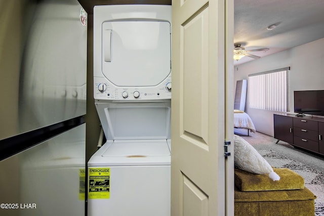 clothes washing area featuring stacked washer / drying machine, a ceiling fan, laundry area, and carpet floors