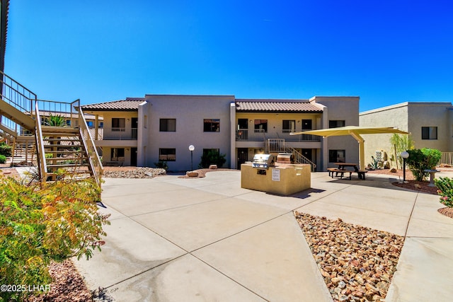rear view of property with stucco siding, stairway, a patio, and an outdoor kitchen