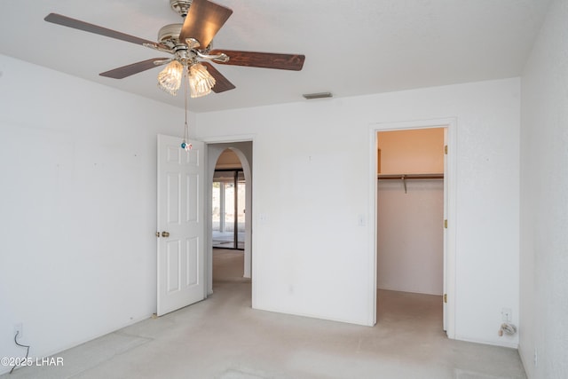 unfurnished bedroom featuring a walk in closet, light colored carpet, a closet, and ceiling fan