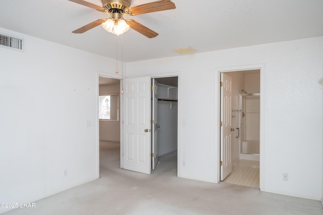 unfurnished bedroom featuring ceiling fan, ensuite bathroom, light carpet, a walk in closet, and a closet