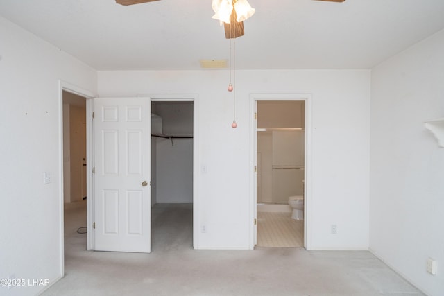 unfurnished bedroom with ceiling fan, ensuite bathroom, a spacious closet, light colored carpet, and a closet