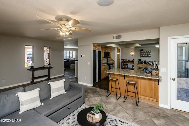 tiled living room featuring a ceiling fan, visible vents, and baseboards